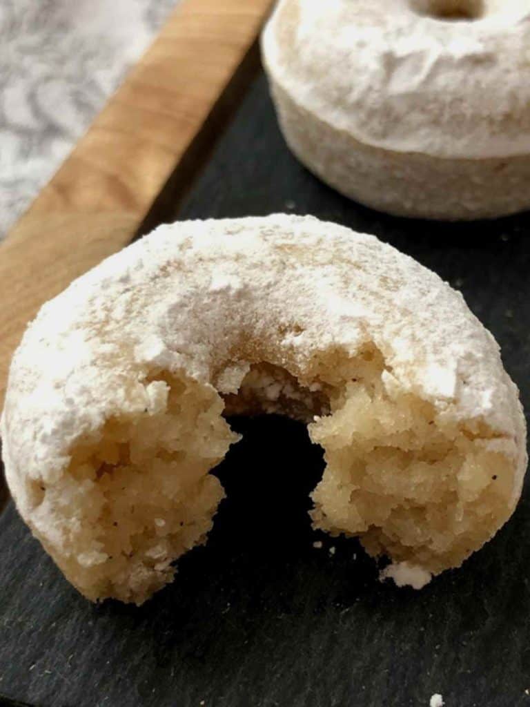 Half a doughnut dusted in powdered sugar on a black board