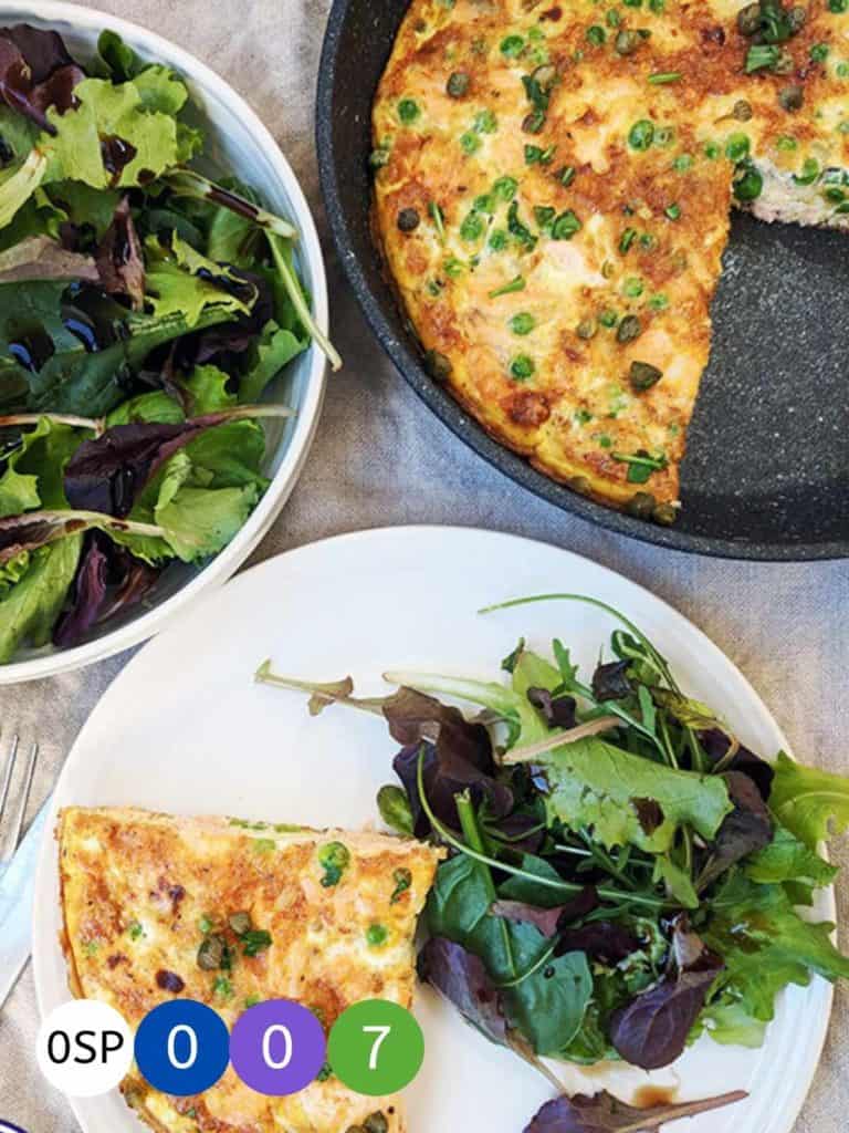 A skillet and plate of salmon & pea frittata with a side salad.