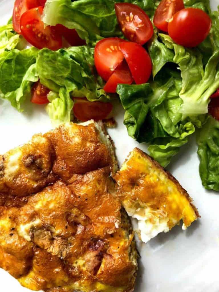 A white plate with a slice of frittata and a green salad.