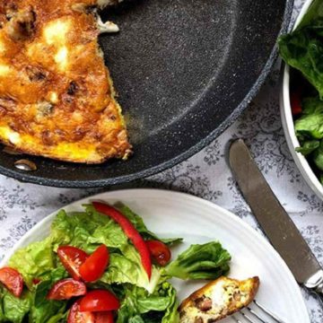 A skillet of frittata with a slice on a plate with a green salad.