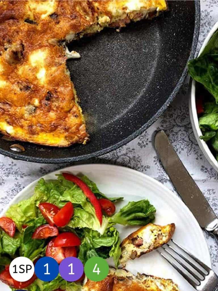 A skillet of frittata with a slice on a plate with a green salad.