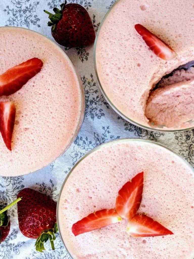 Three dishes of pink strawberry fluff with sliced strawberries on top.