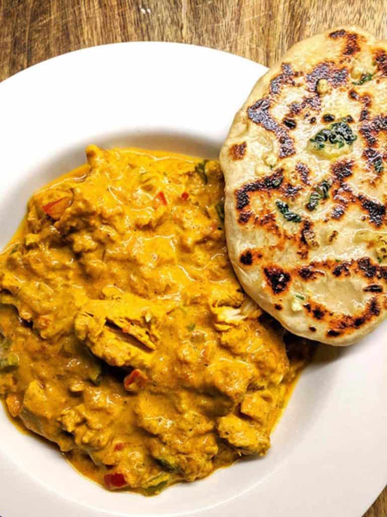 A white bowl full of chicken tikka masala and a naan bread.