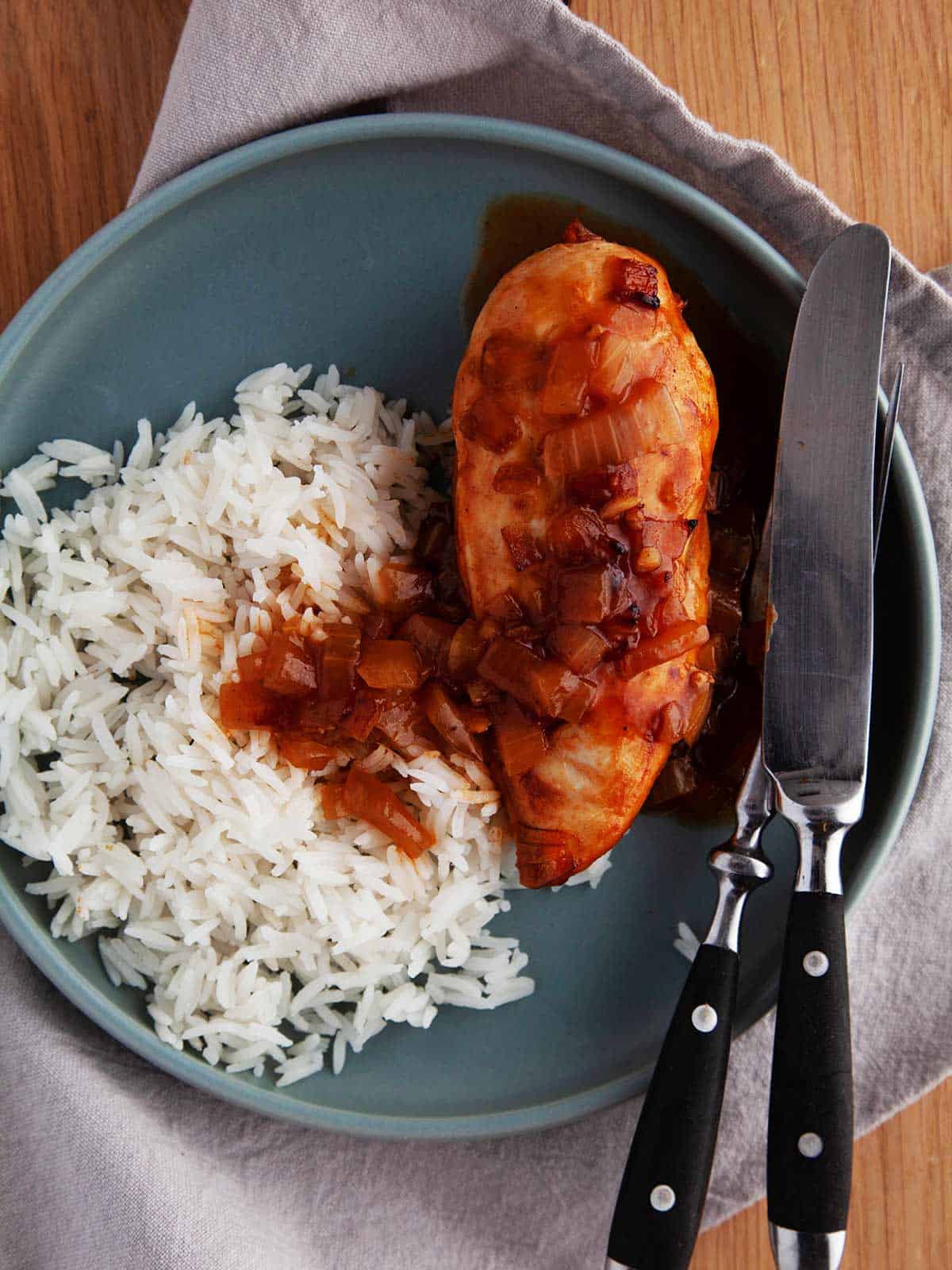 A blue plate on a linen napkin with white rice and chicken in ginger beer sauce.