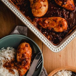 A dish of chicken casserole on a wooden table with a plate of chicken and rice.