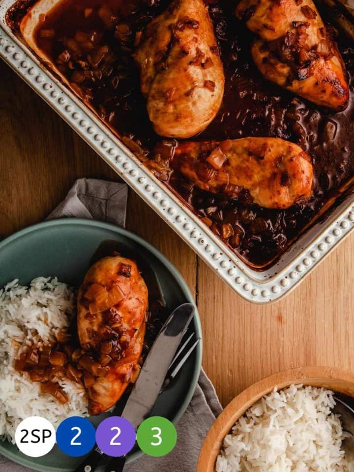 A dish of chicken casserole on a wooden table with a plate of chicken and rice.