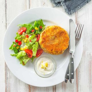 A white plate with a fishcake and some salad on a white wooden table.