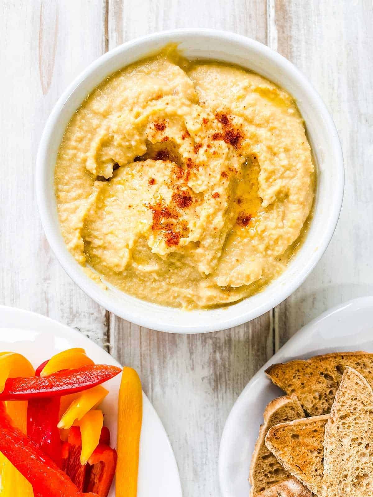 A bowl of Weight Watchers hummus with a plate of sliced pepper and some toasted bread.