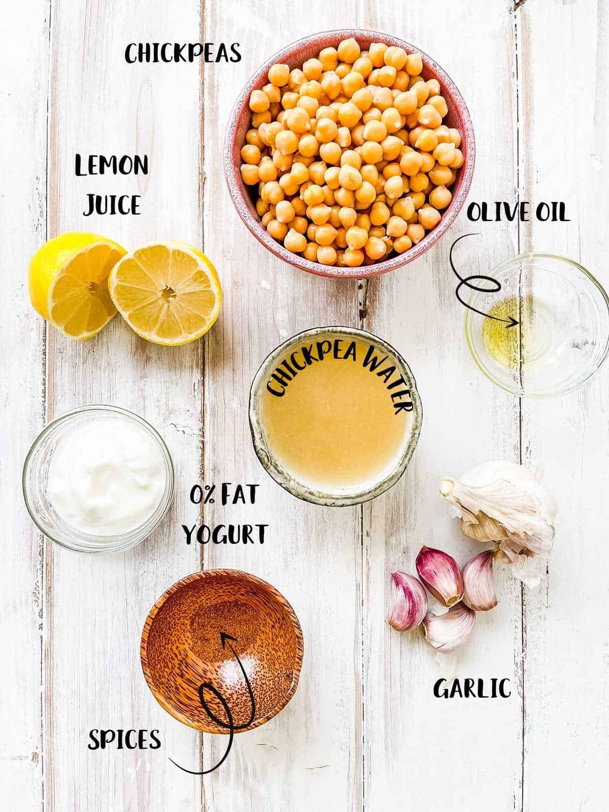 Bowls of the ingredients needed to make hummus for Weight Watchers on a white table with text labels.