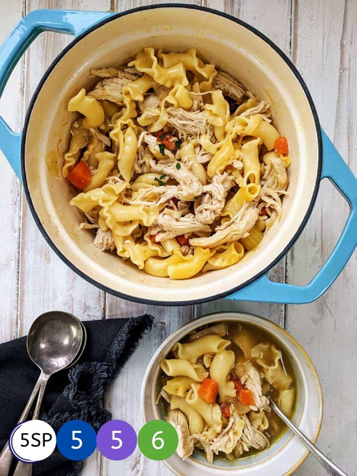 A blue casserole dish of chicken and noodles on a white wooden table.