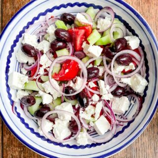 A blue and white bowl full of Greek salad on a wooden table.