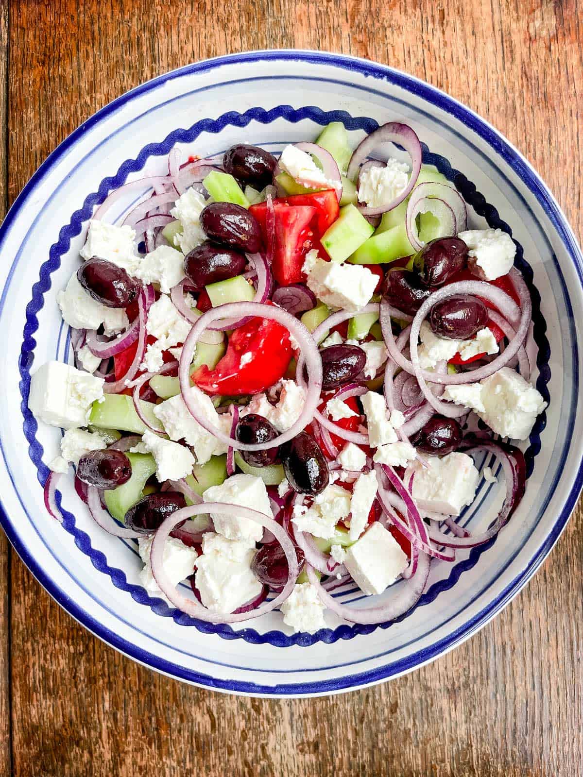 A blue and white bowl full of Greek salad on a wooden table.