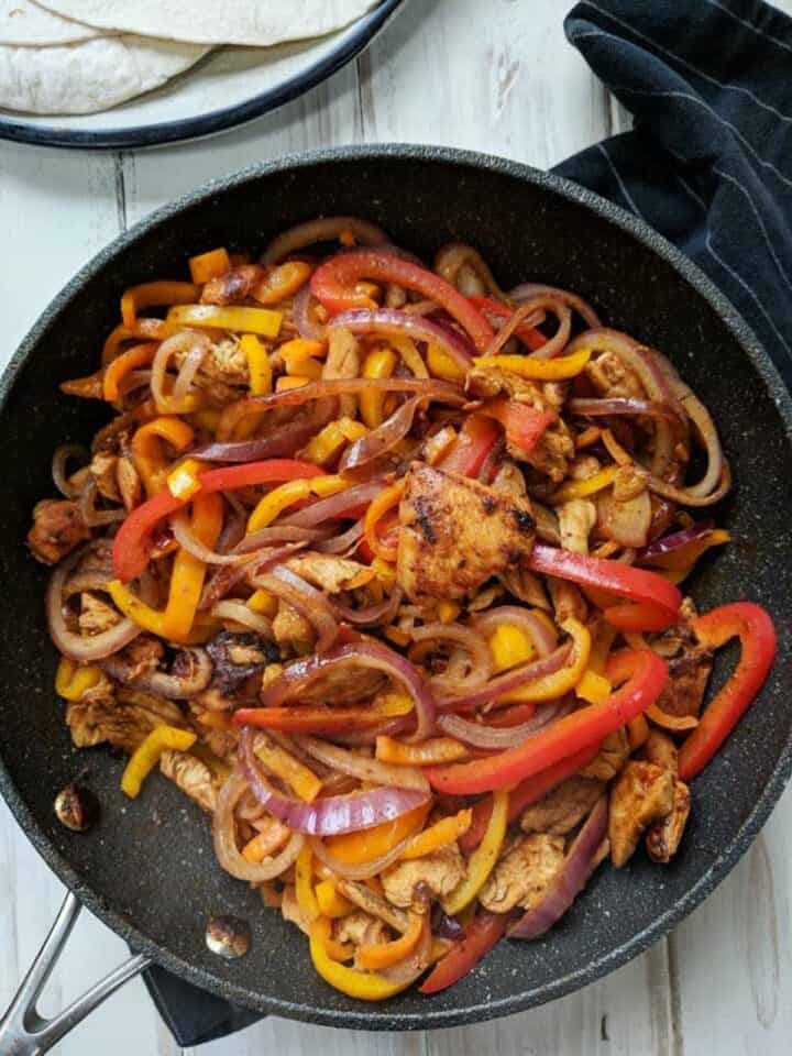 A skillet of chicken fajita mix on a white table.