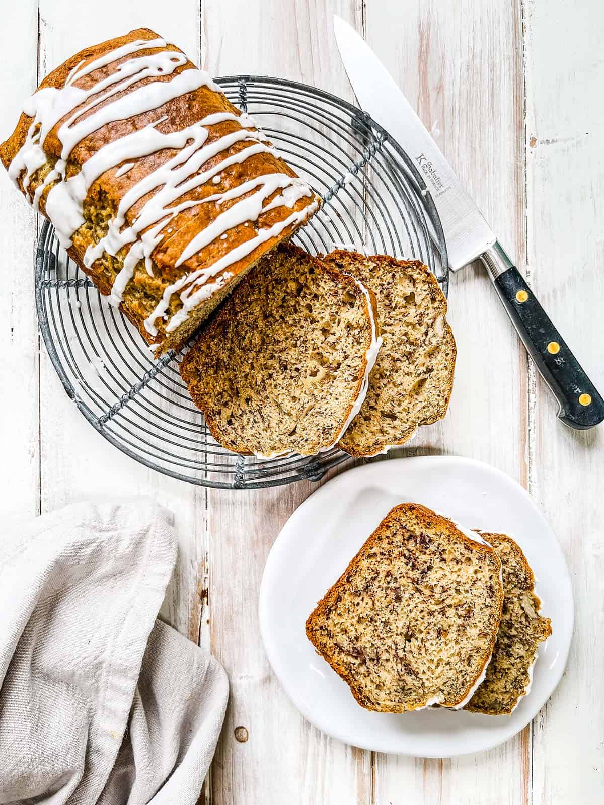 A loaf of sliced banana bread on a wire rack on a white table.