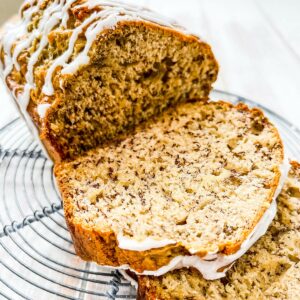 A loaf of sliced banana bread on a wire rack on a white table.