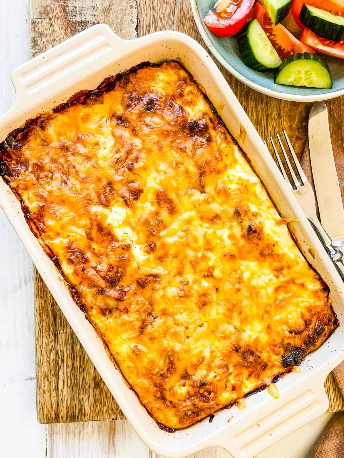 A baked casserole on a wooden board with a side dish on the side.