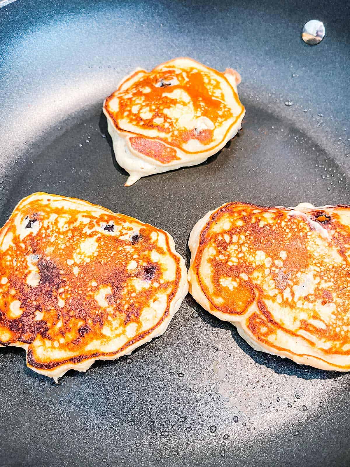 Three pancakes cooking in a skillet.