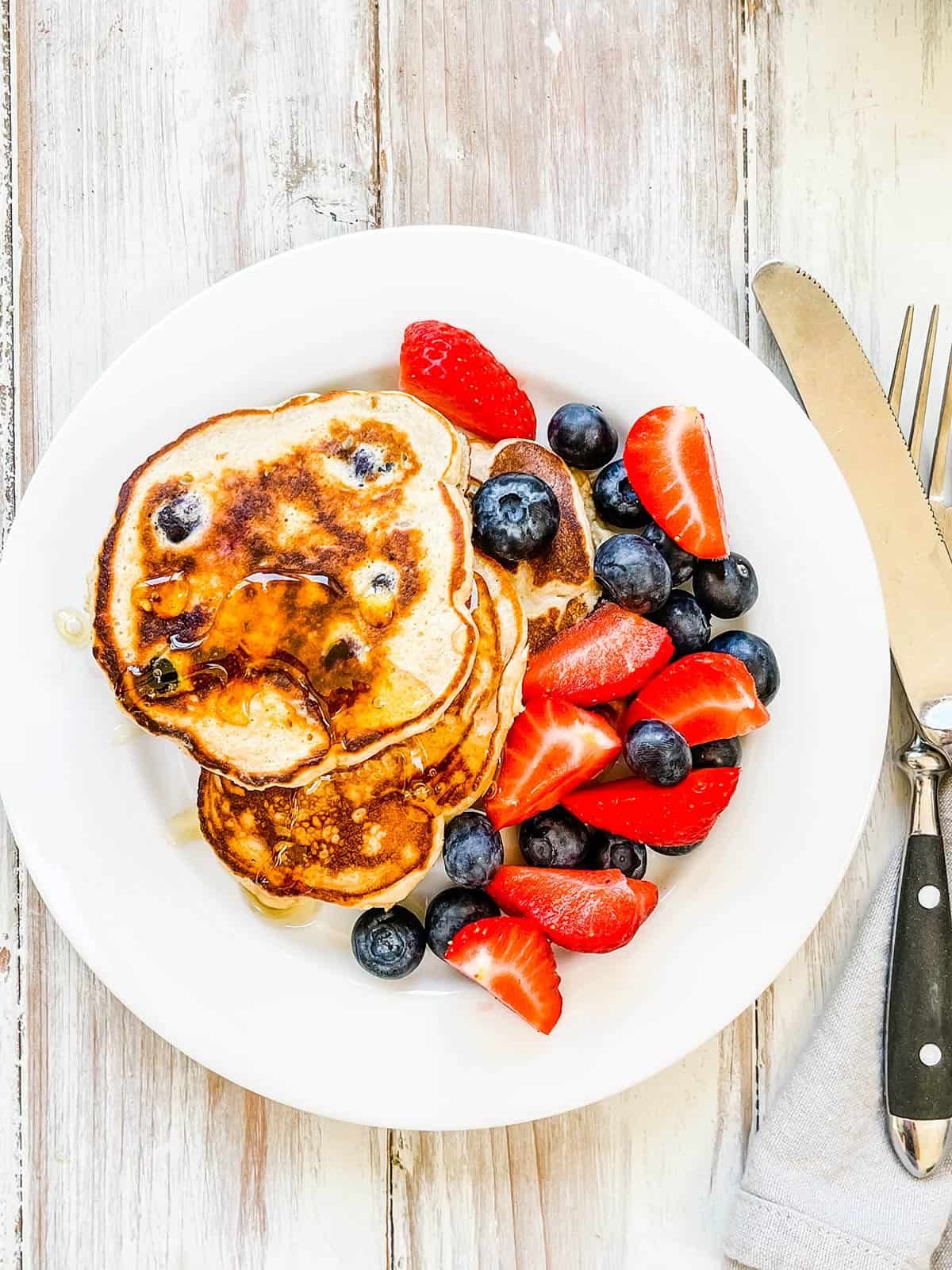 A plate of pancakes with mixed berries on a white table.