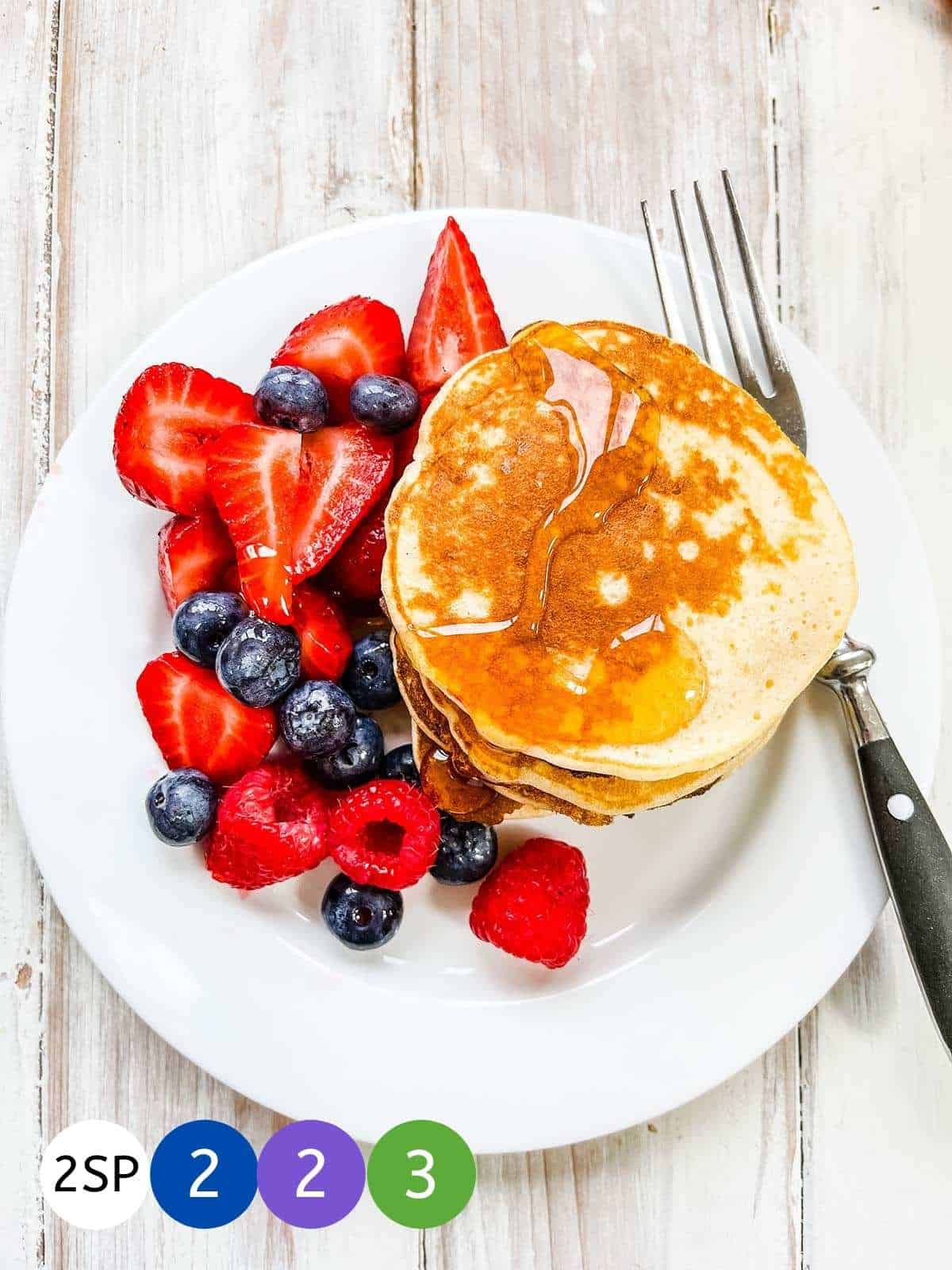 A white plate of pancakes and berries with coloured markers signifying WW SmartPoints.