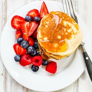 A white plate with a stack of pancakes and syrup and mixed berries.