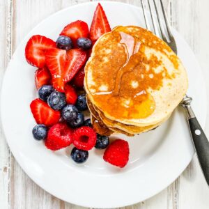 en vit tallrik med en stapel pannkakor och sirap och blandade bär.