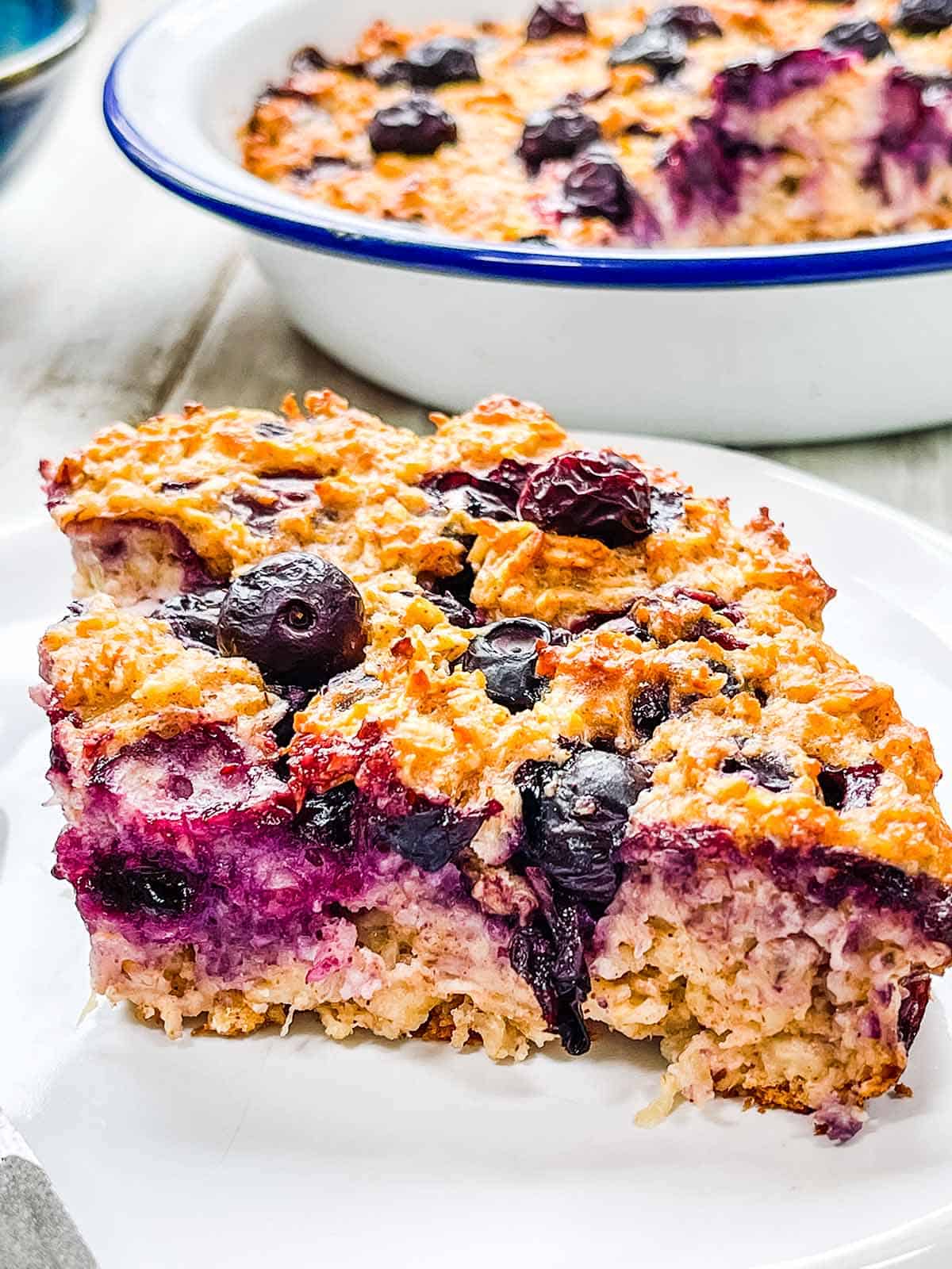 A white plate on a white table with blueberry baked oatmeal.