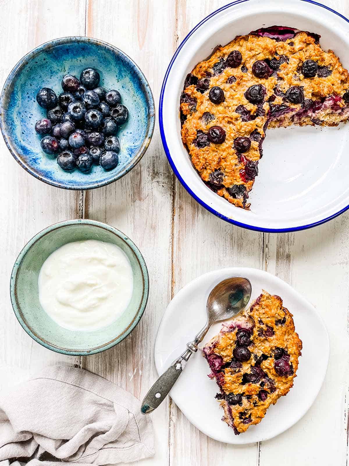 A white table with a dish of baked oatmeal and blueberries.
