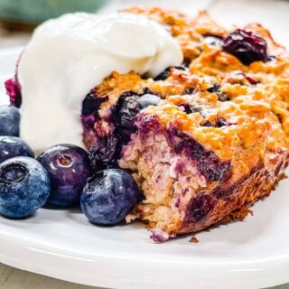 A white plate with baked oatmeal and blueberries and yogurt.
