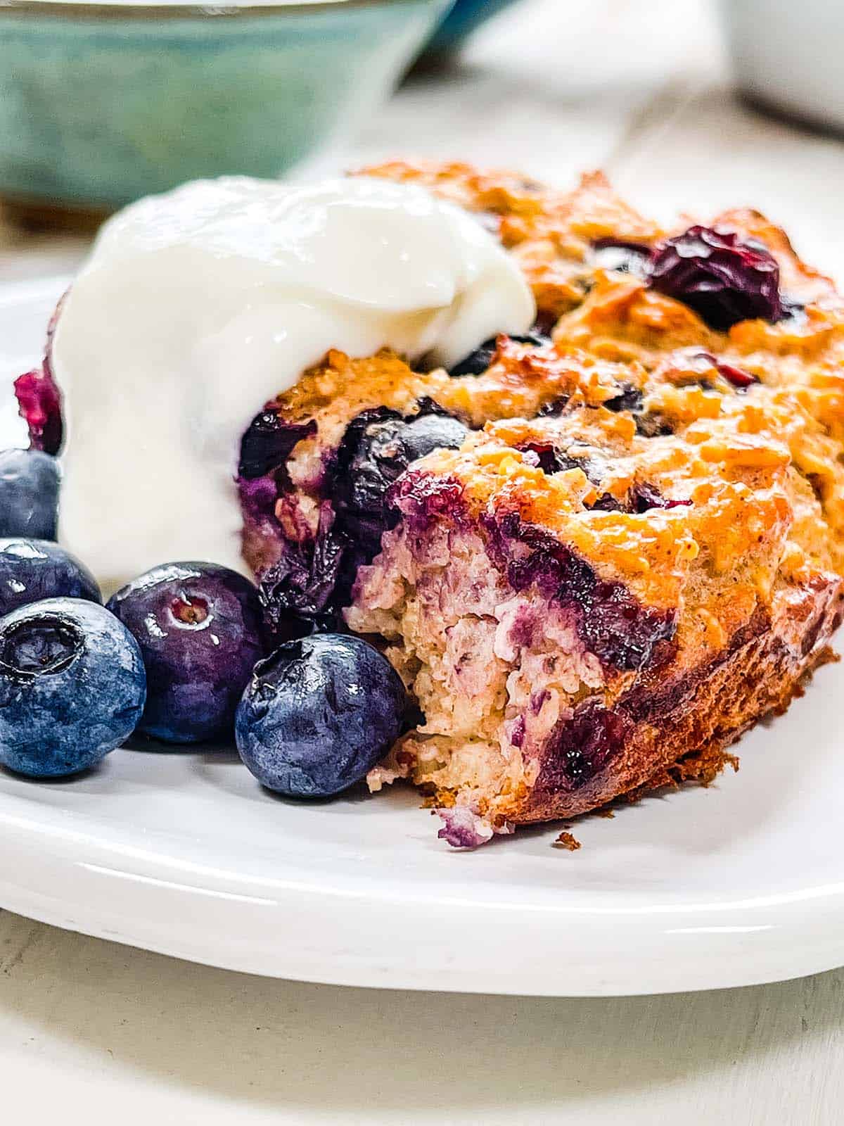 A white plate with baked oatmeal and blueberries and yogurt.