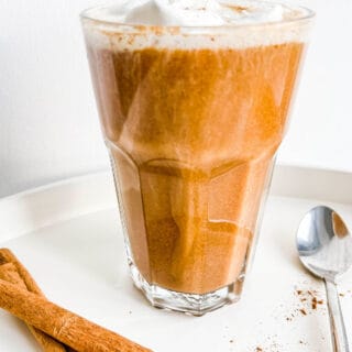 A glass full of coffee and topped with cream with cinnamon sticks.
