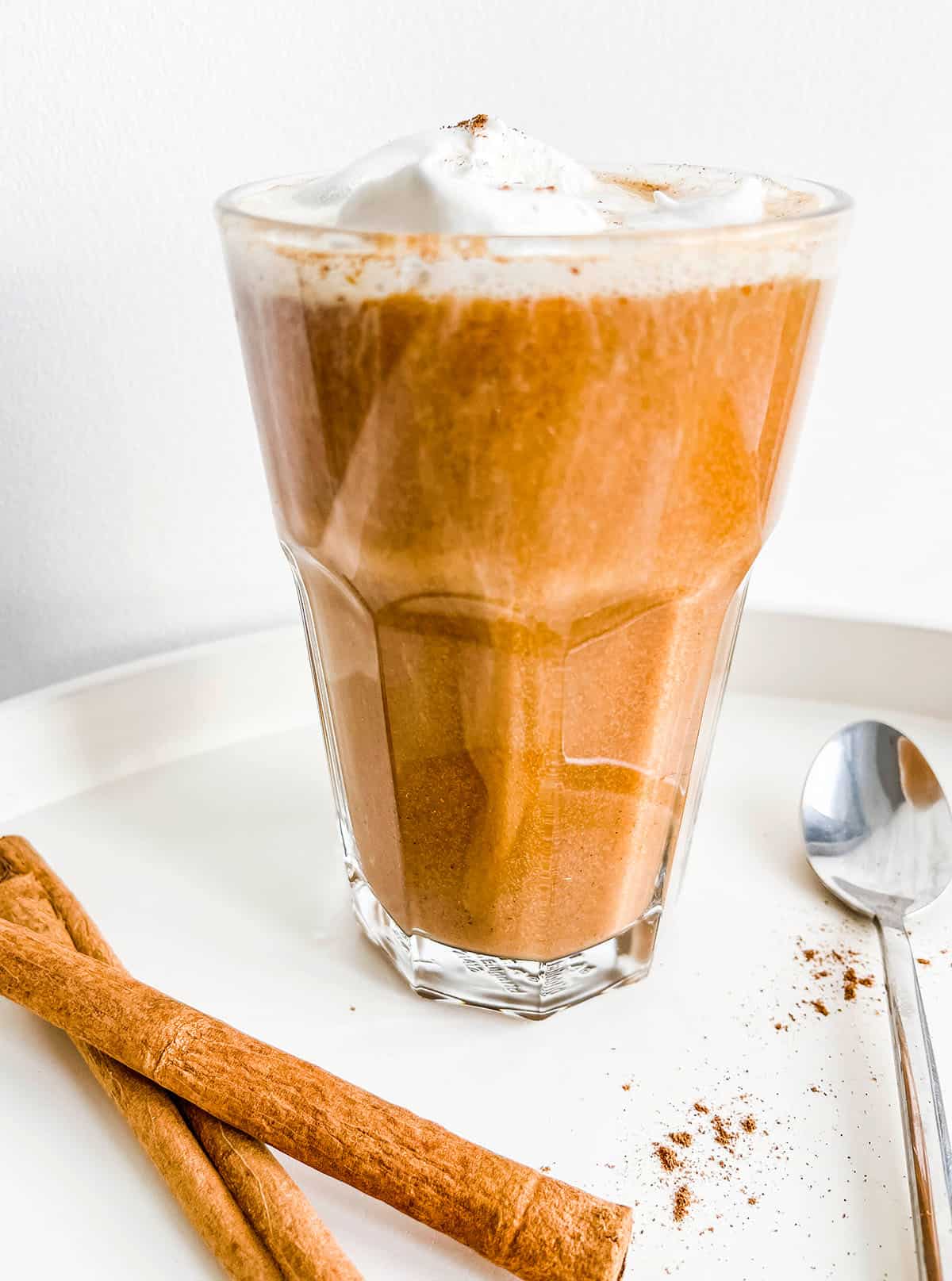 A glass full of coffee and topped with cream with cinnamon sticks.