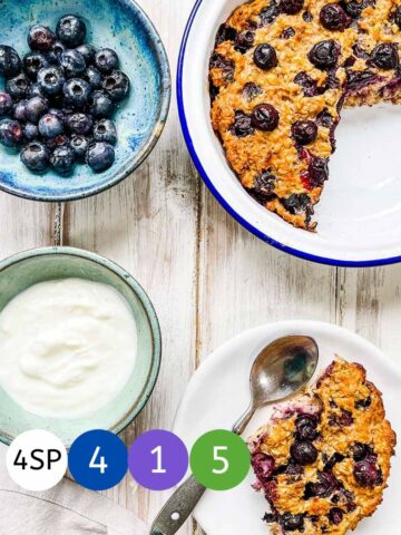 A dish of baked oatmeal on a white table with dishes of blueberries and yogurt.