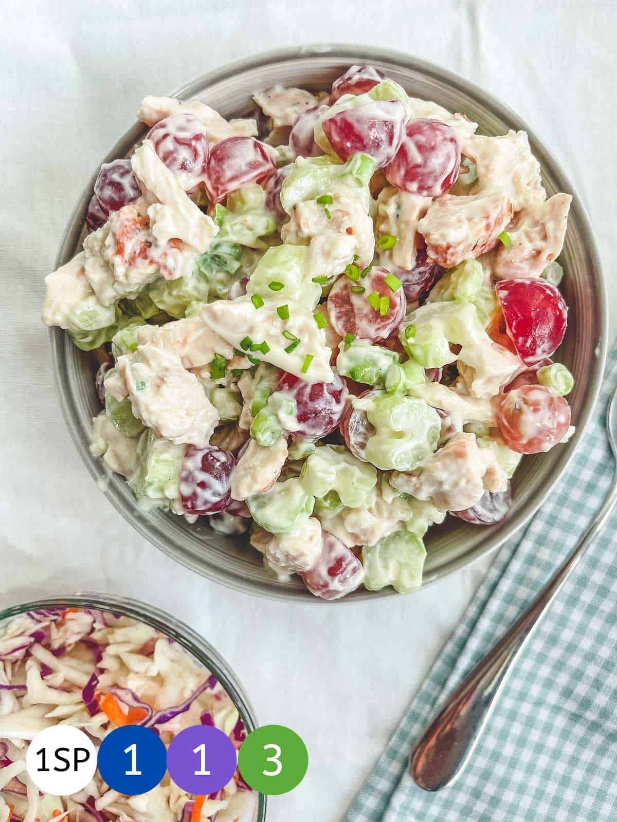 A bowl of chicken salad on a white table with coloured circles showing Weight Watchers SmartPoints