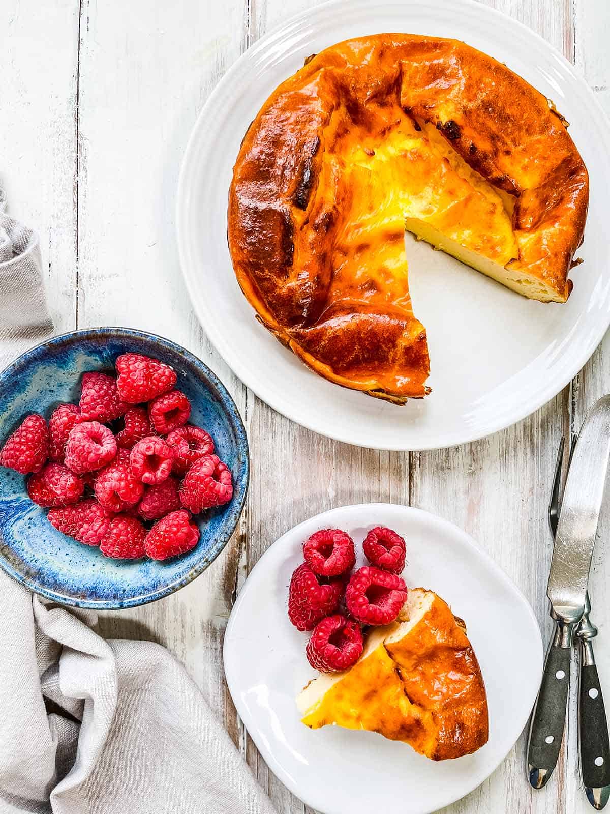 A tart on a white table with a bowl of raspberries.
