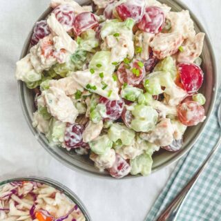 A bowl of chicken salad on a white table with a checkered napkin.