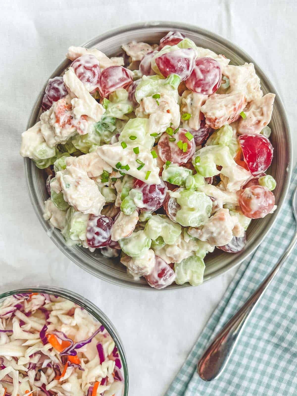 A bowl of chicken salad on a white table with a checkered napkin.