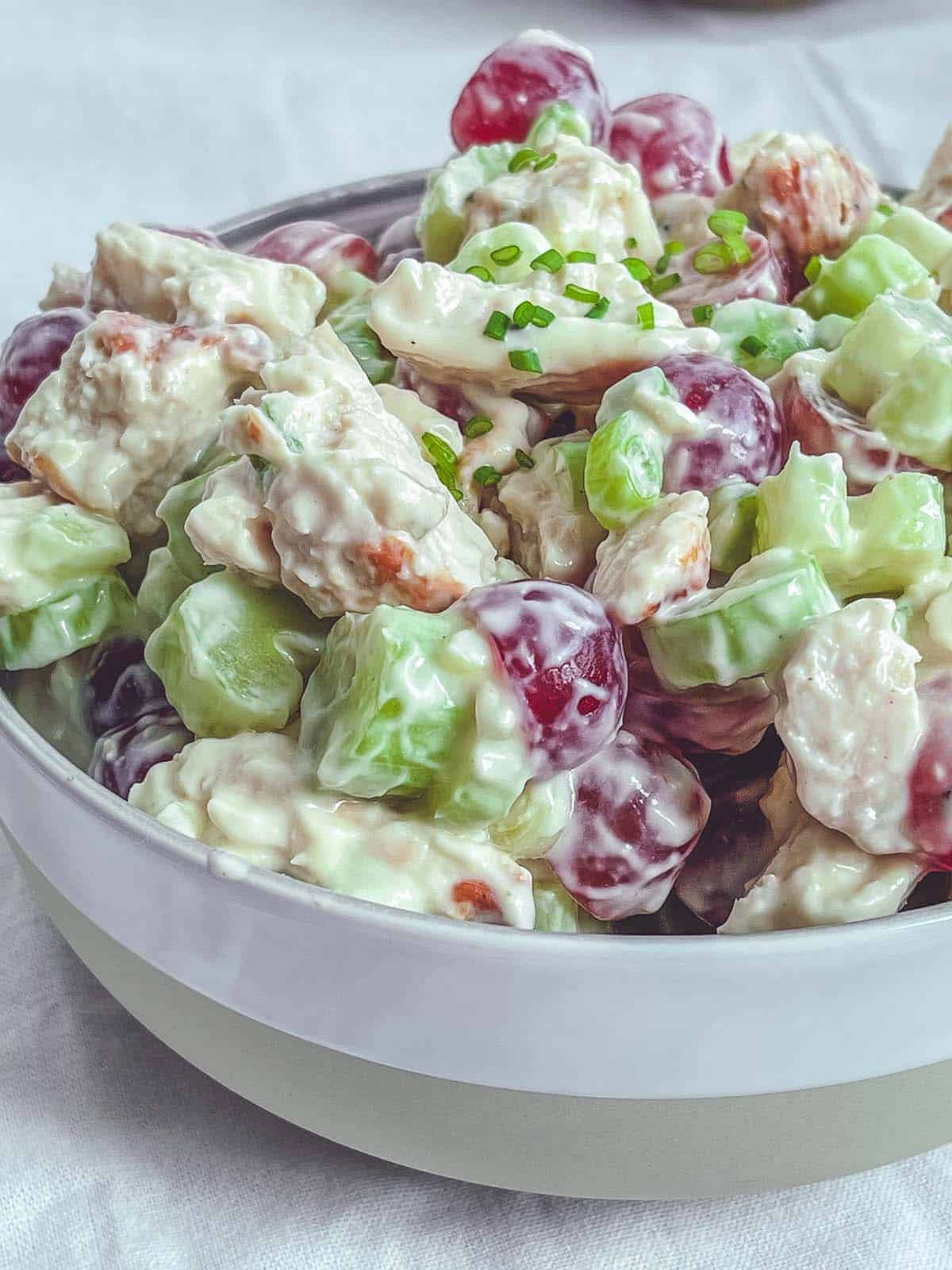 A close up photos of a bowl of chicken salad on a white table.