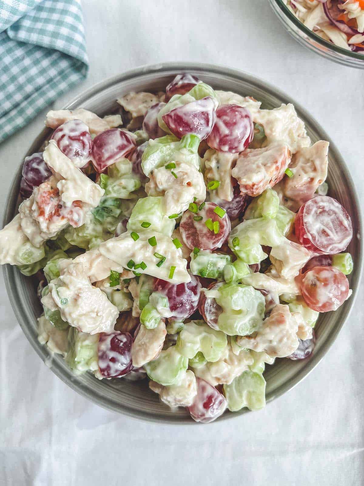 A bowl of chicken salad on a white table with a checkered napkin.