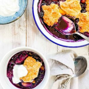 A dish of peach and blueberry cobbler on a white table.