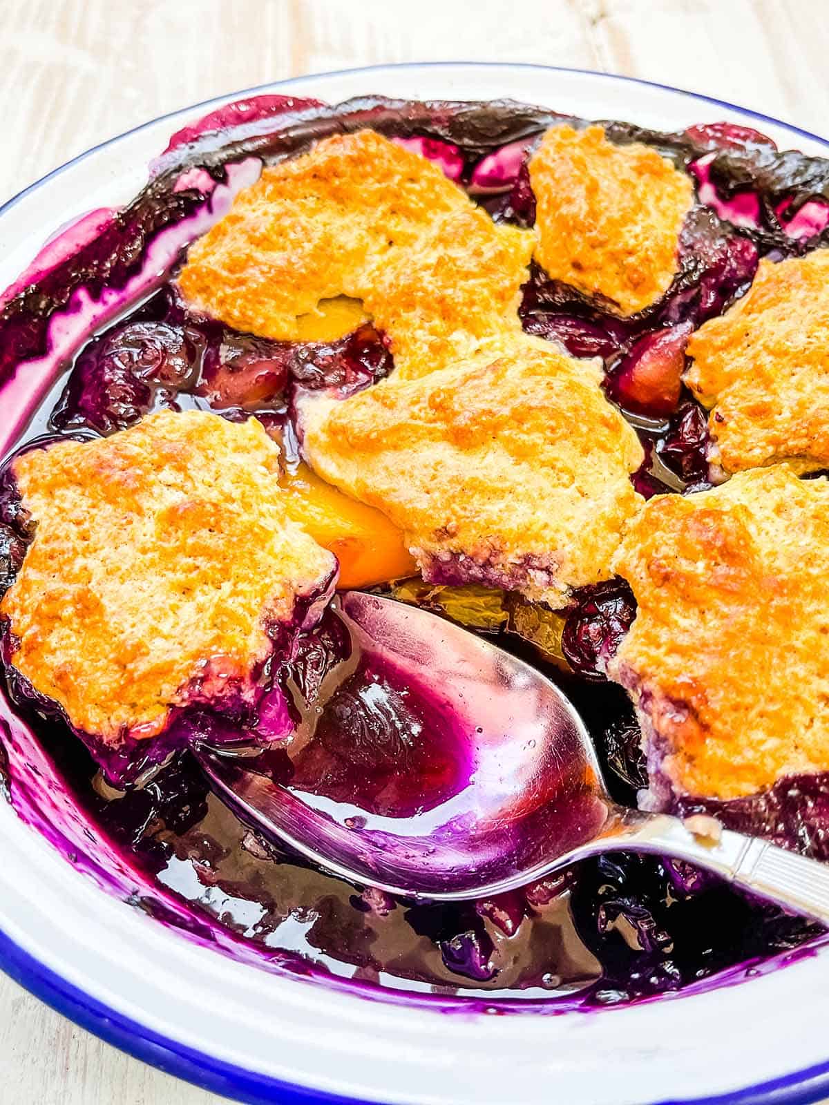 A close up picture of a dish of blueberry and peach cobbler.