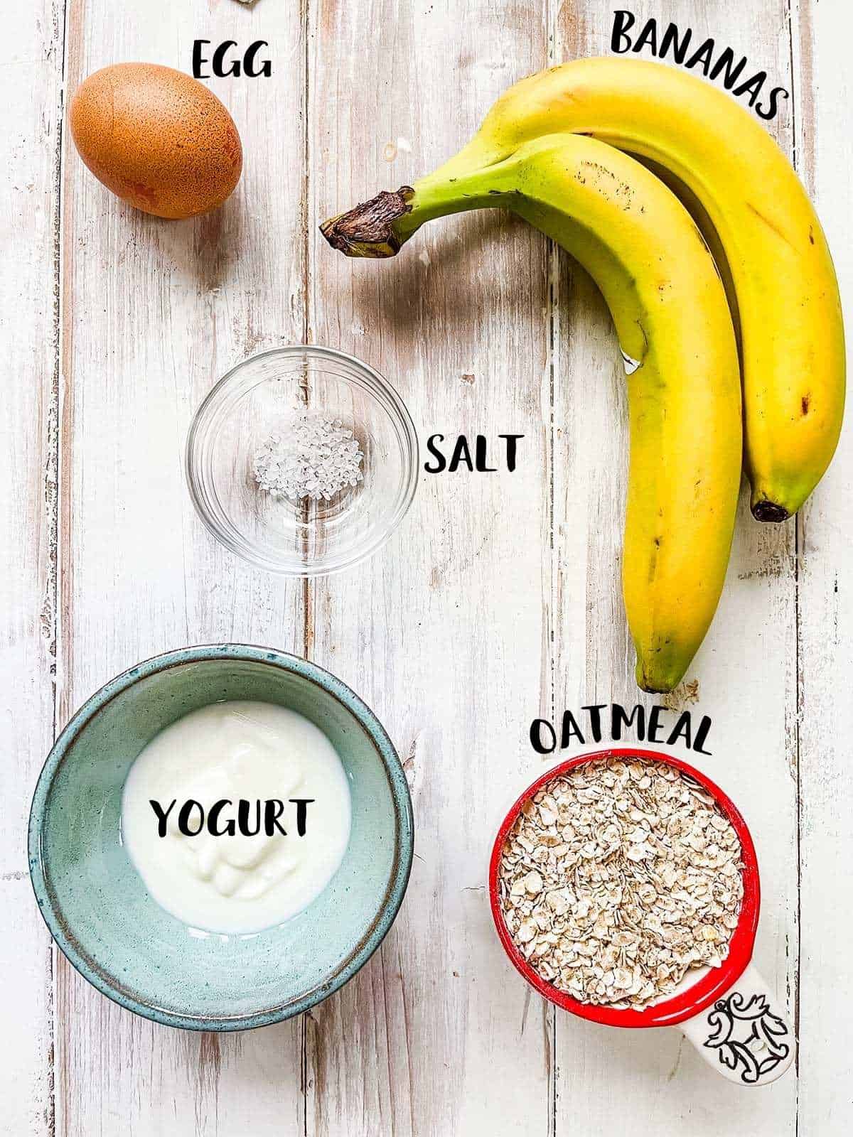 Ingredients to make banana pancakes laid out on a white table with labels.
