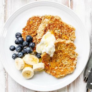 A white plate with banana oatmeal pancakes topped with berries and sliced banana.