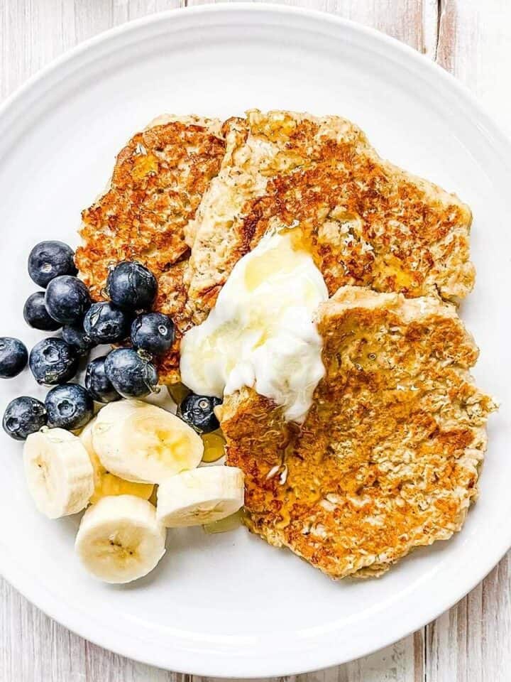 A white plate with banana oatmeal pancakes topped with berries and sliced banana.