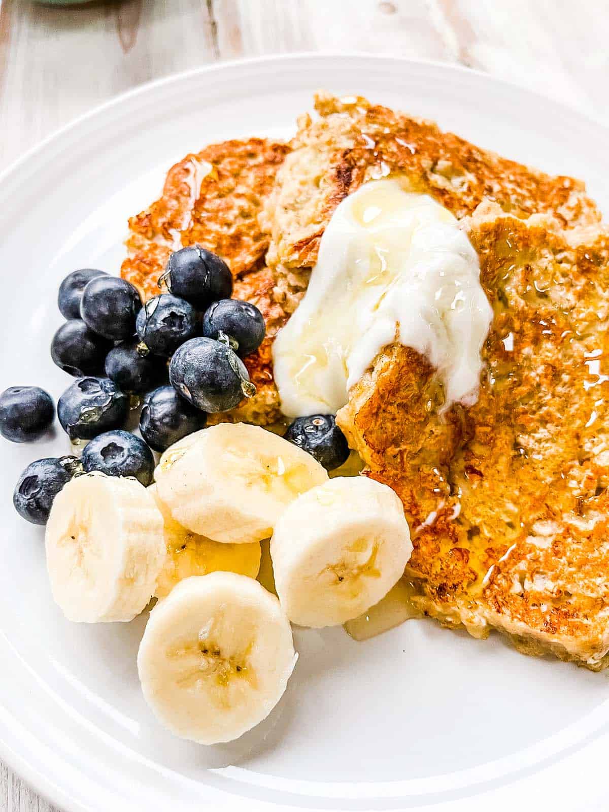 A white plate with banana oatmeal pancakes topped with berries, yogurt and sliced banana.