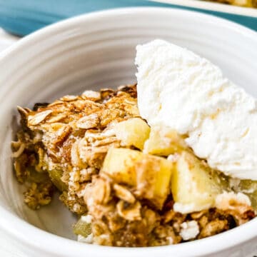 A white dish full of baked oatmeal with apples and topped with cool whip.