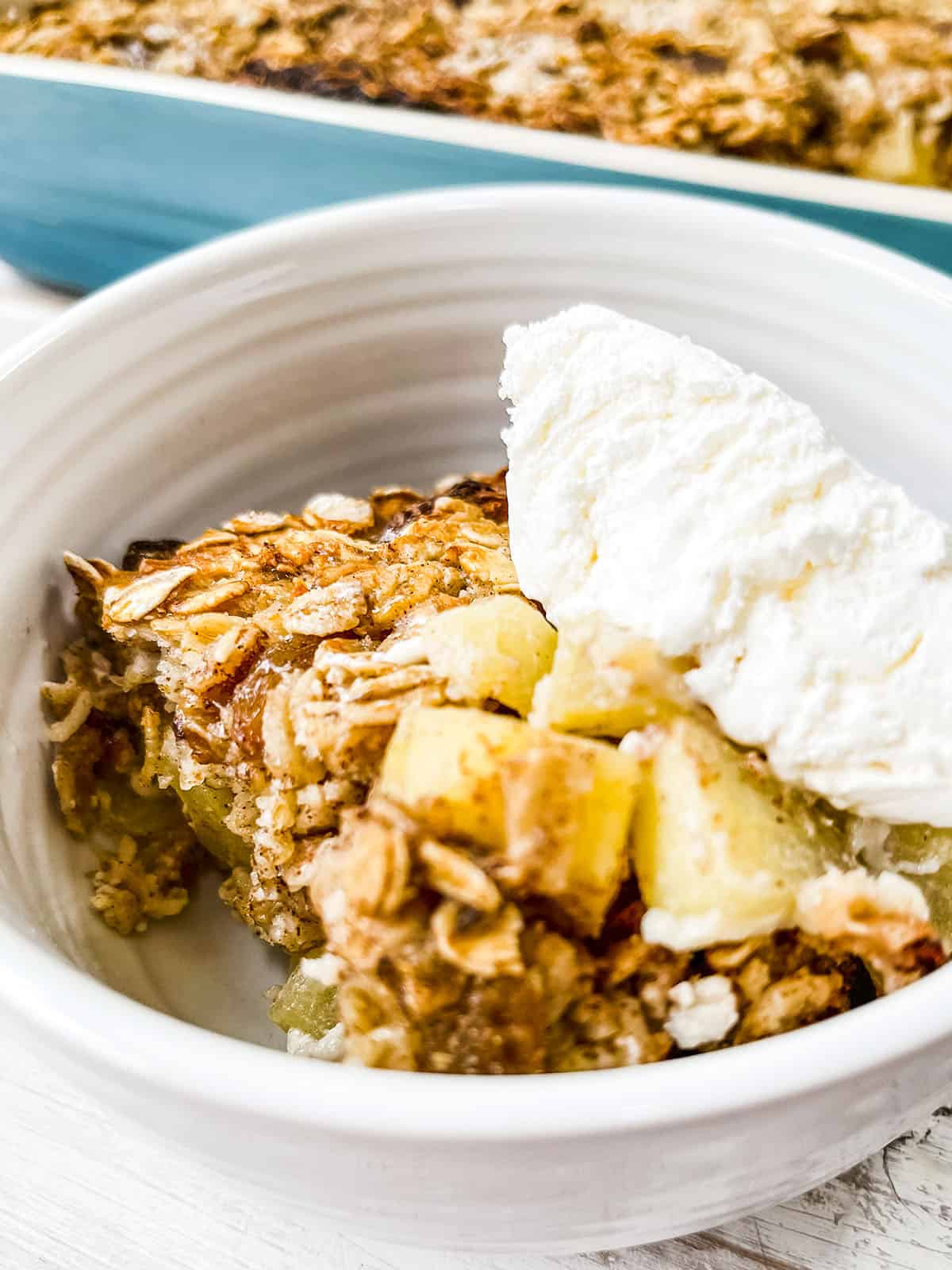 A white dish full of baked oatmeal with apples and topped with cool whip.