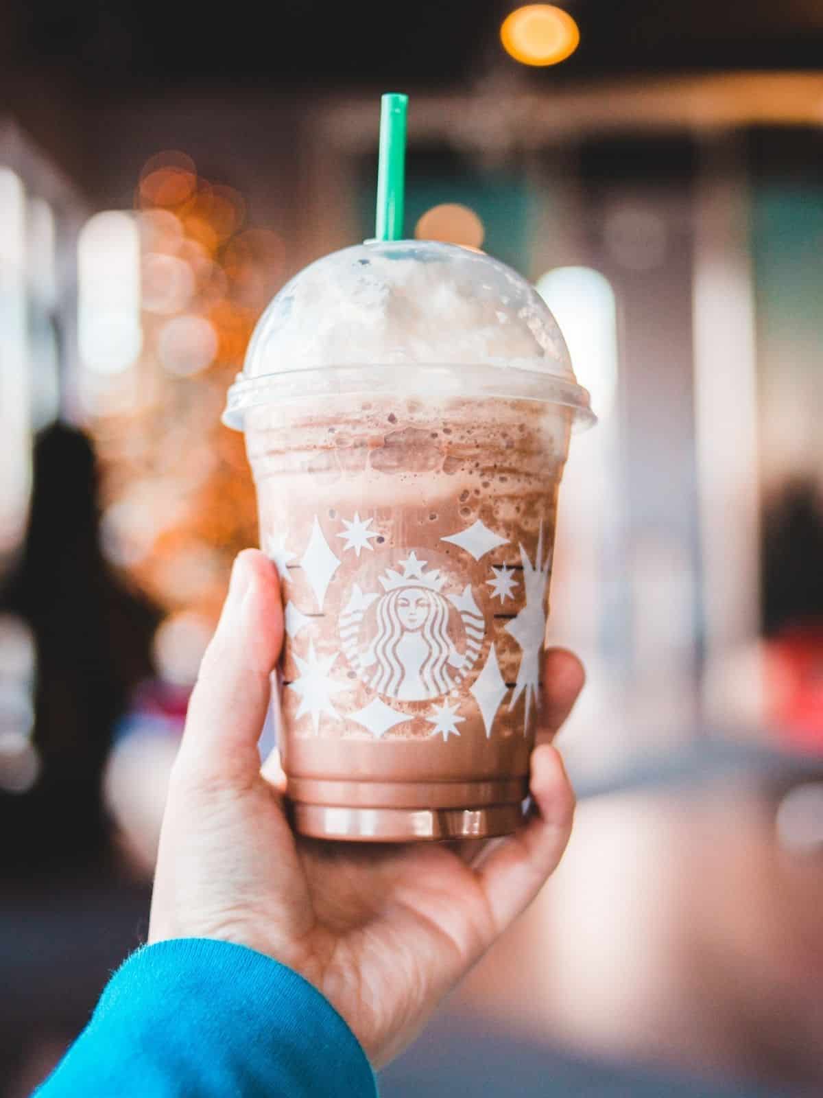 A hand holding a starbucks drink with a straw.