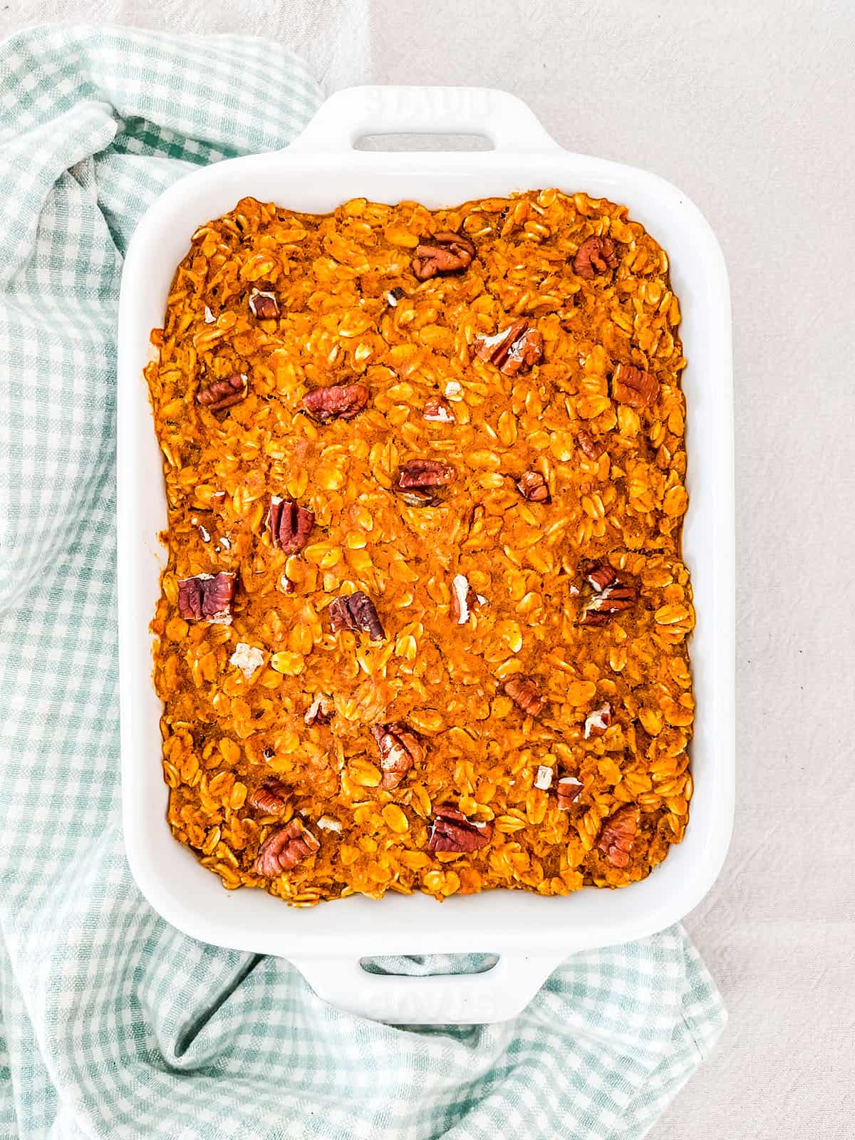 A dish of baked oatmeal topped with pecan nuts on a white table.