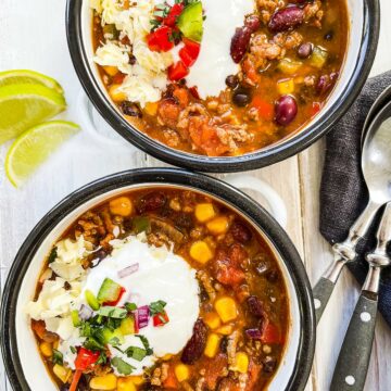 Two white and black dishes full of taco soup on a white wooden table.