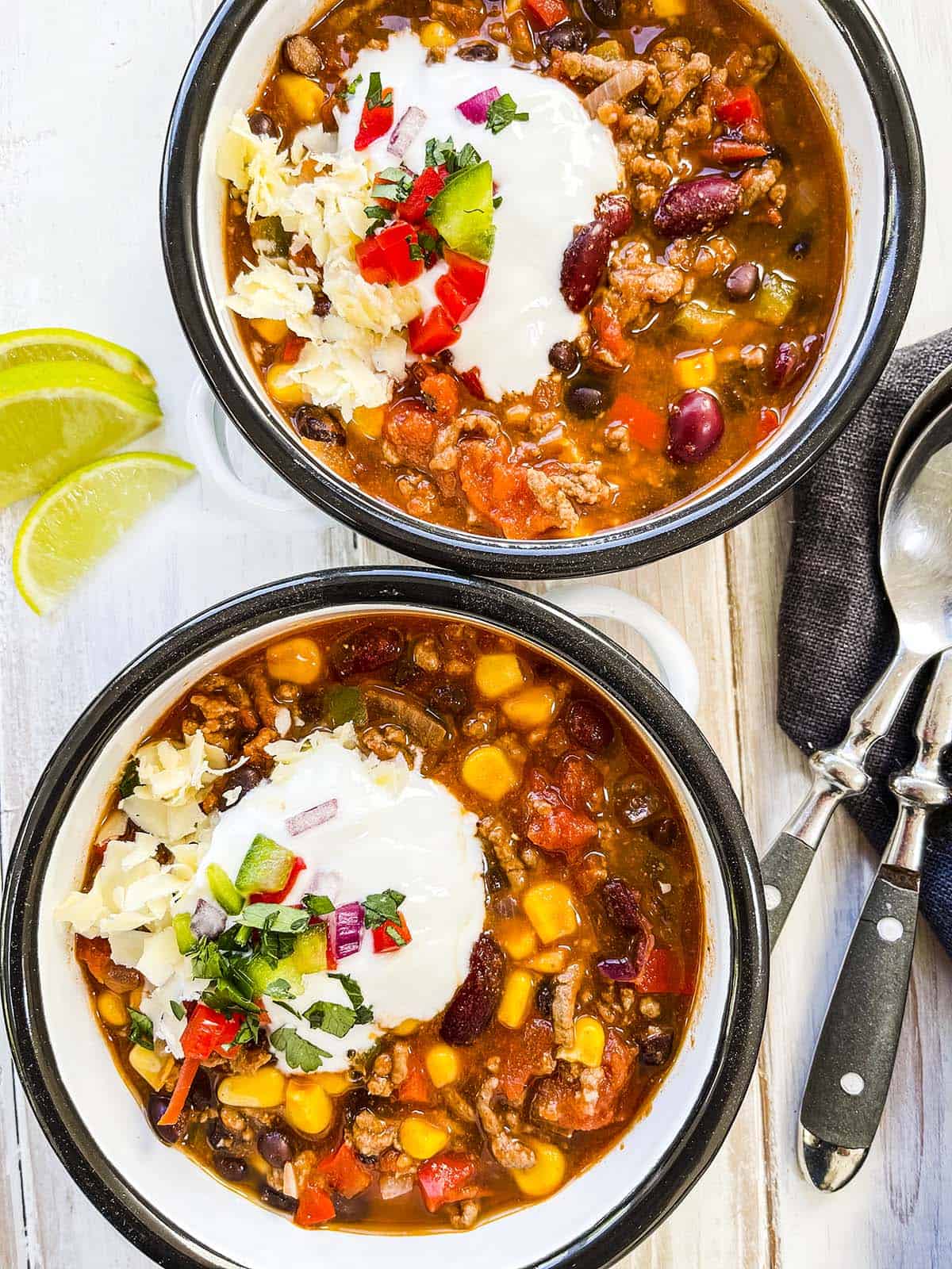 Two white and black dishes full of taco soup on a white wooden table.